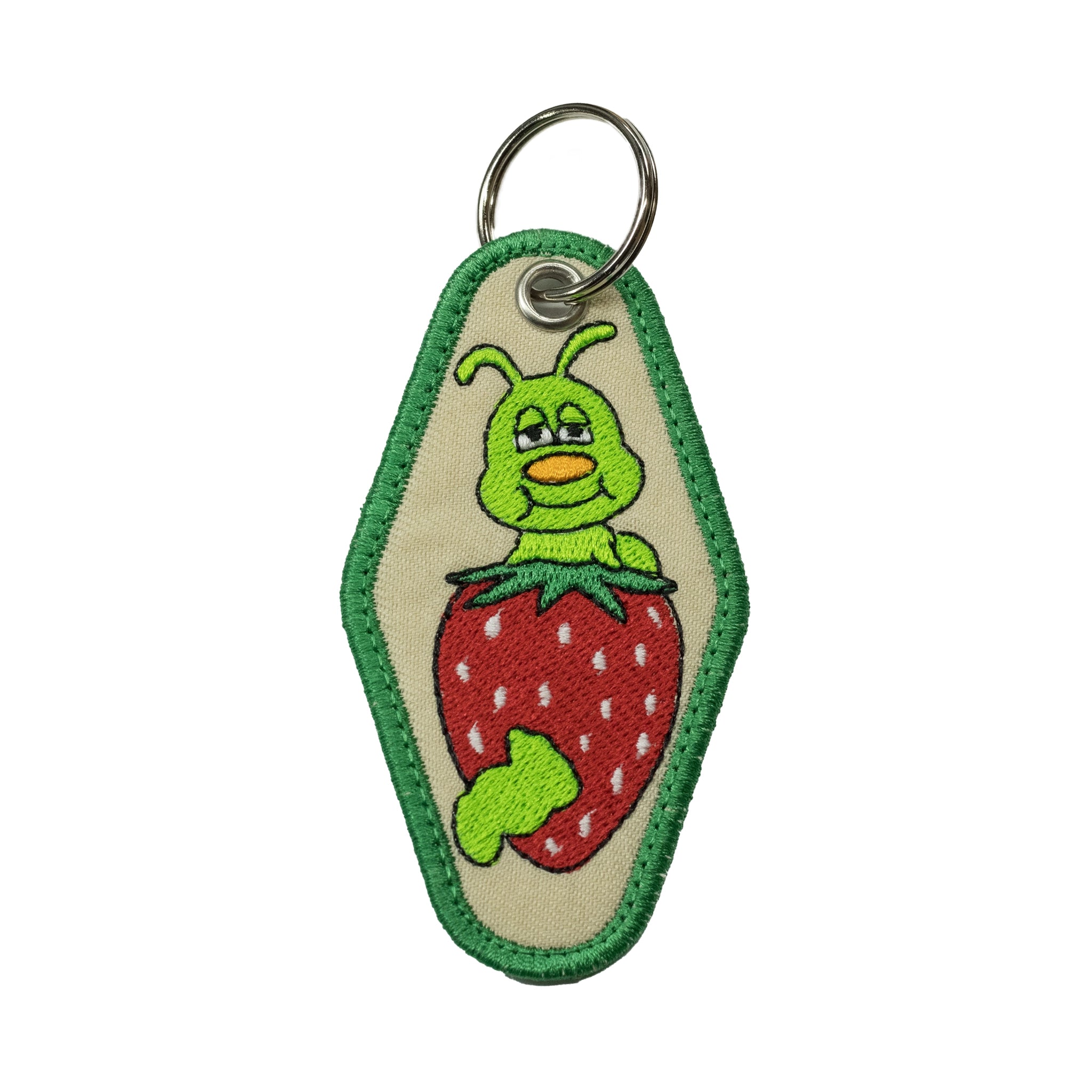 Front view of a beige diamond-shaped motel keychain by Regular Magic featuring an embroidered green caterpillar character emerging from a red strawberry.