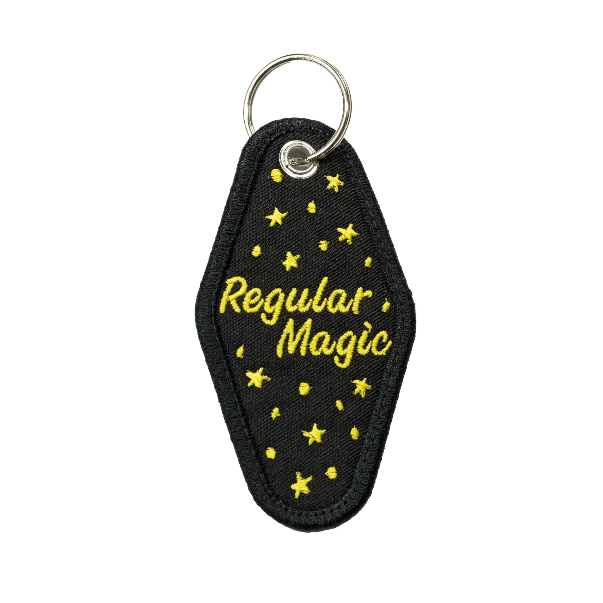Back view of a black diamond-shaped motel keychain by Regular Magic featuring yellow embroidered 'Regular Magic' script surrounded by stitched yellow stars.