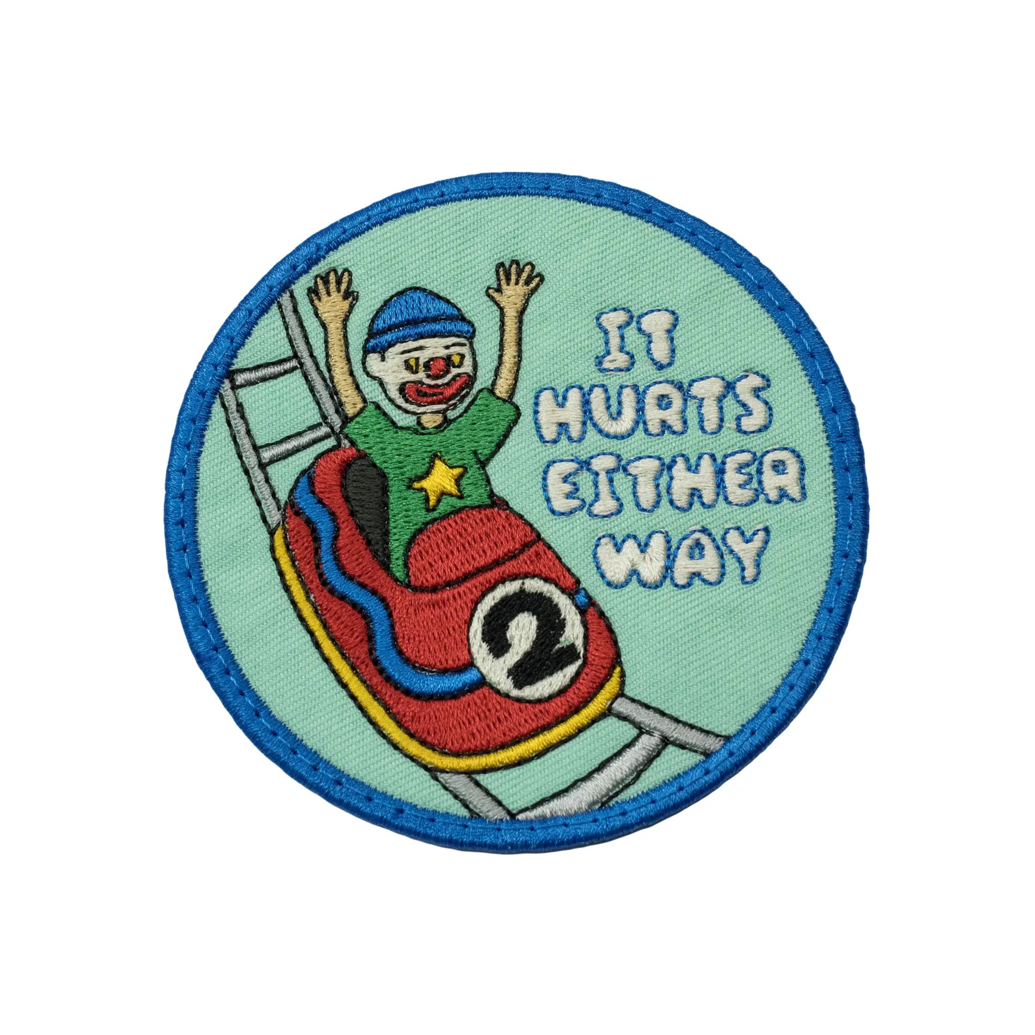 Circular mint green embroidered patch by Regular Magic featuring a clown character riding a rollercoaster cart with arms raised, accompanied by blue stitched text that reads 'IT HURTS EITHER WAY'.