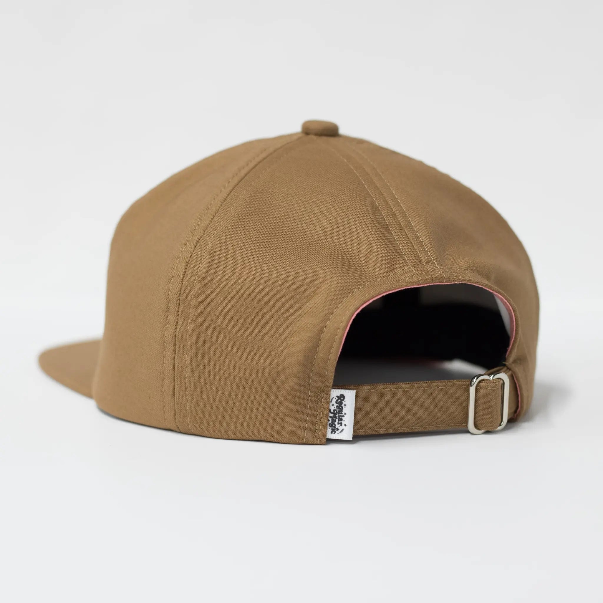 Back view of a brown Regular Magic cap showing the matching fabric strap, silver metal slider buckle, and  Regular Magic brand label tag at the rear opening.