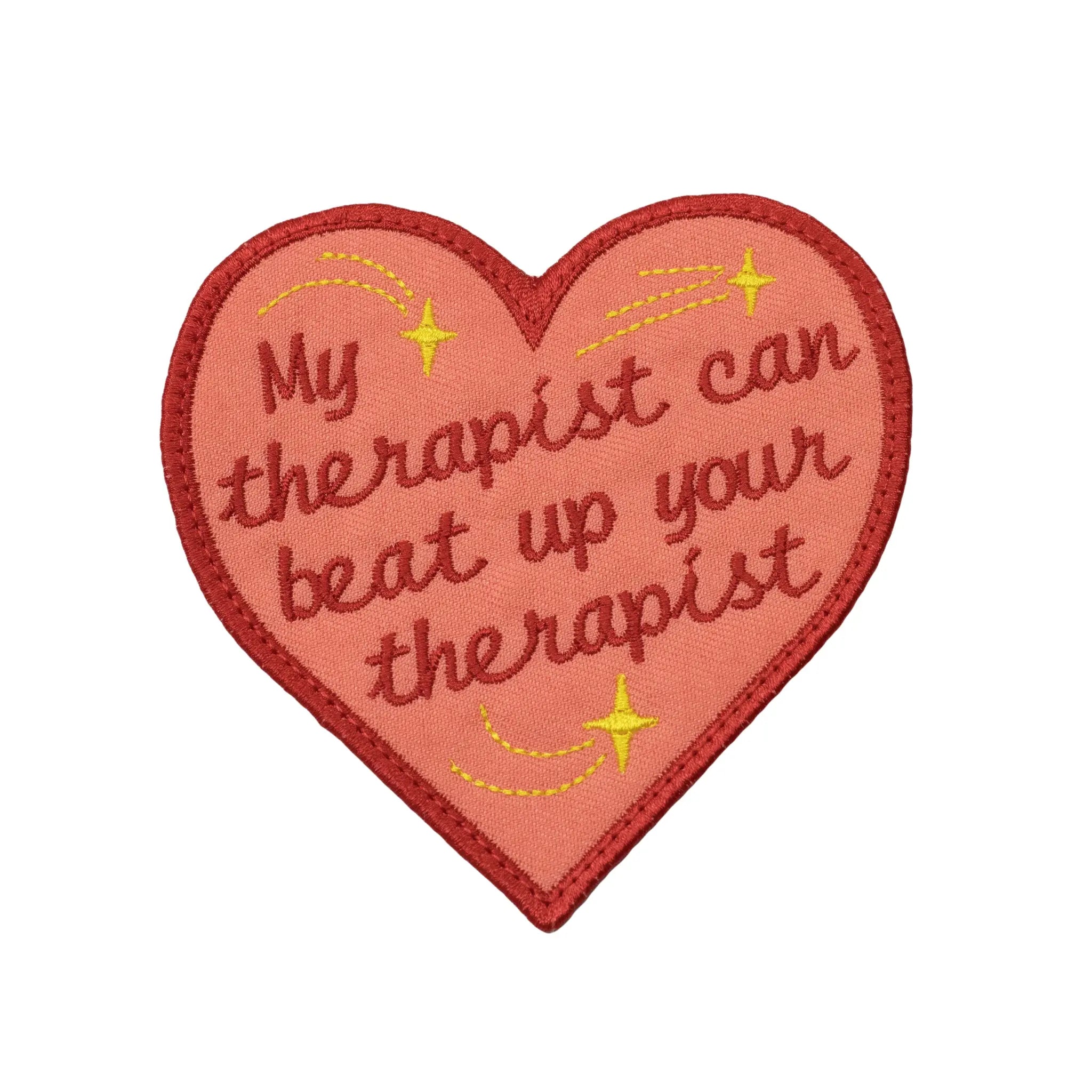 Pink heart-shaped embroidered patch by Regular Magic featuring dark red cursive text reading 'My therapist can beat up your therapist' with yellow stitched shooting stars and a red border.