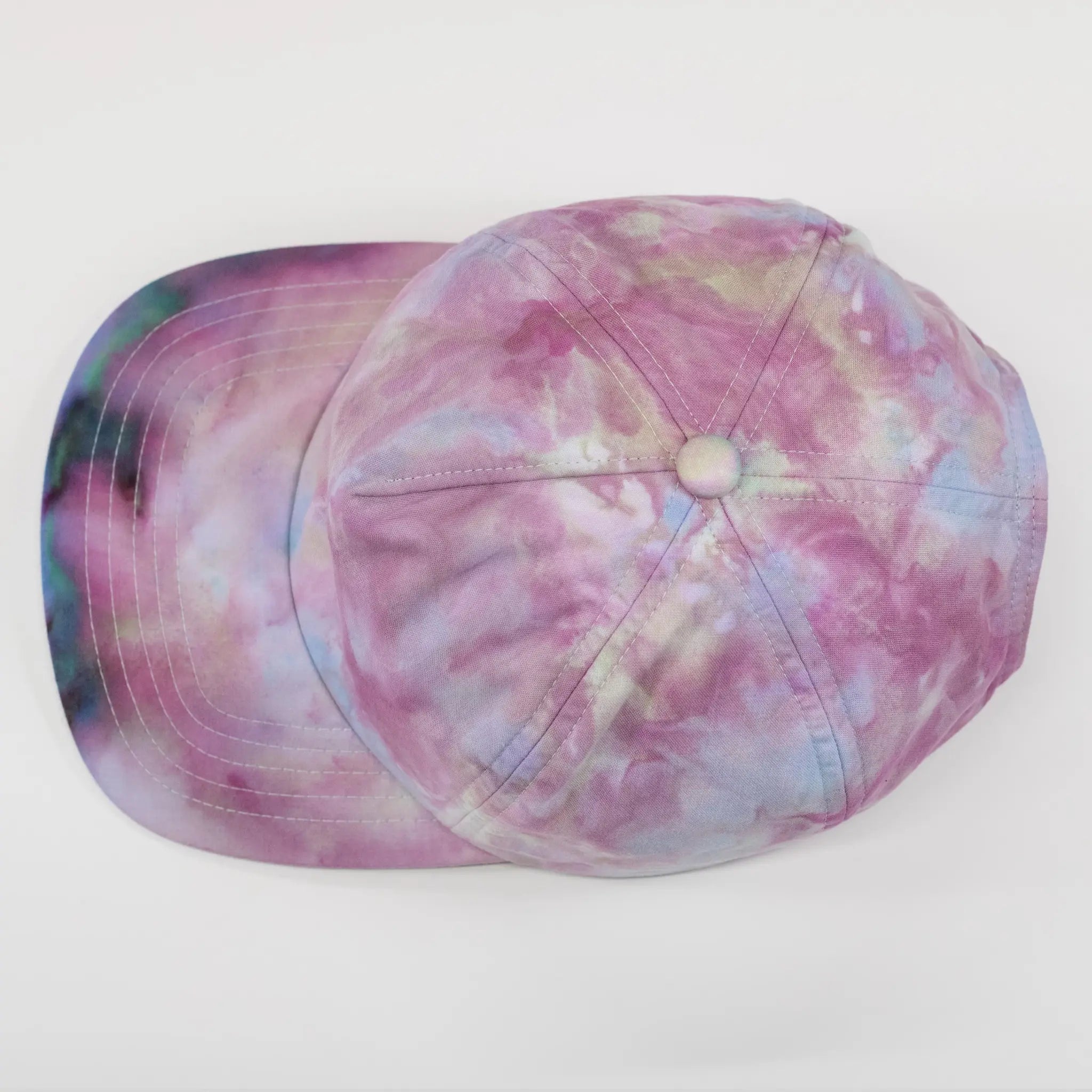 Top-down view of a Regular Magic pastel tie-dye 6-panel cap displaying the full pink, purple, and blue ice dye swirl pattern across the crown and brim.